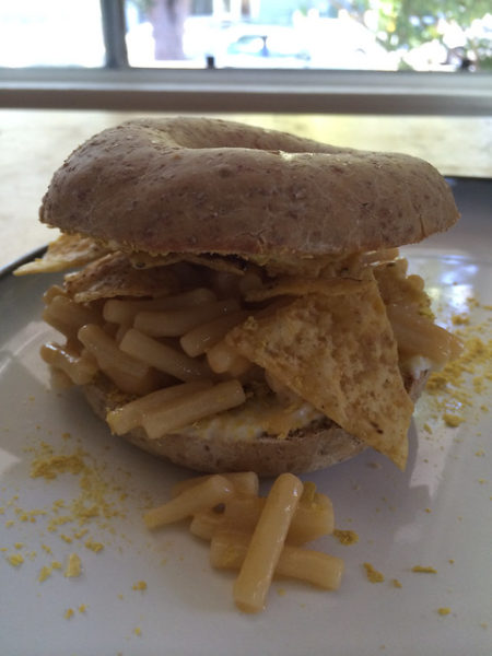 A bagel sandwich with macaroni and cheese, and corn chips