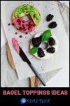 An open faced bagel with cream cheese, berry, avocado, and pomegranate toppings