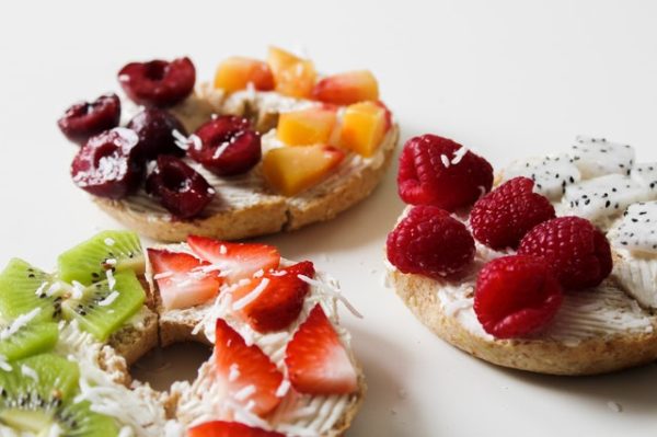 Bagels smeared with cream cheese and topped with different fruits and shredded coconut