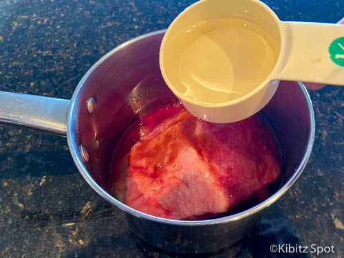 Pouring vinegar over meat in saucepan