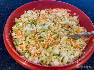 A bowl of our dairy free coleslaw ready to eat. It rests on a wooden block with a side of white sauce