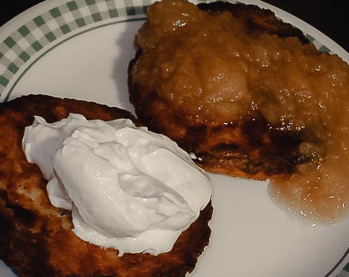 Two latkes on a plate, one topped with applesauce, the other with sour cream