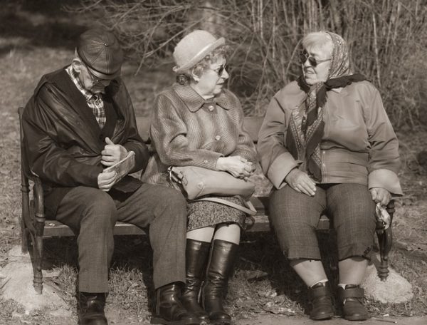 Two older women talking while the man on the bench sleeps. 