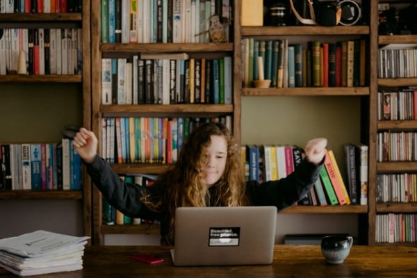 Girl at computer looking accomplished with arms in the air