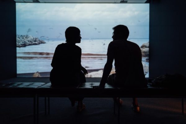 two people practicing conversational Hebrew on a bench with a photo of the beach in the background