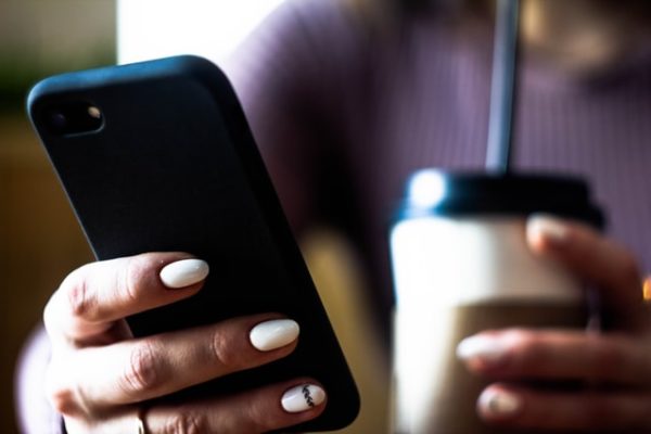 one hand holding a mobile phone, the other a coffee