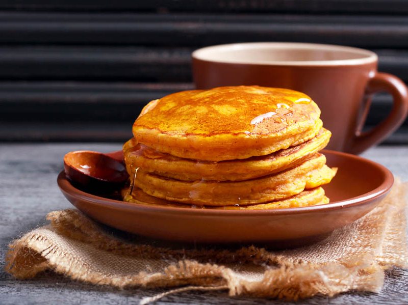 A stack of butternut squash pancakes on a plate topped with syrup