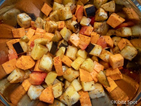 Potatos, eggplant, spices, and olive oil in a bowl