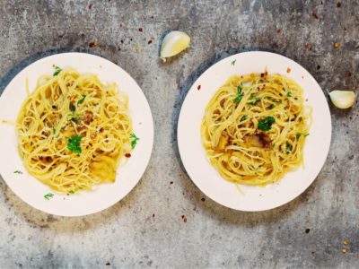 Two plates of garlic spaghetti with cloves of garlic off to the side