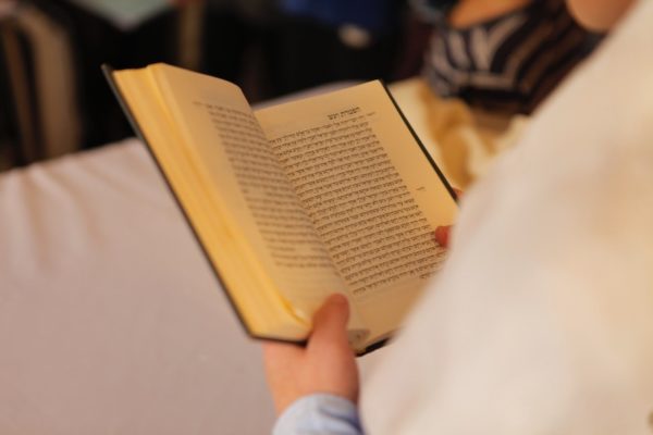 A person holding and reading a machzor during high holiday prayer, perhaps at their prayer space at home