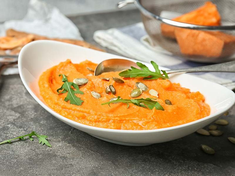 A freshly made pumpkin mash recipe in a white bowl, topped with green herbs