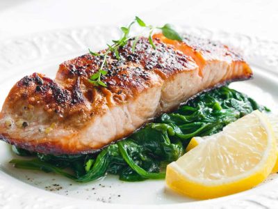 Baked salmon and spinach with a side of lemon on a white plate