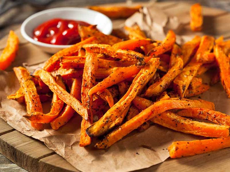 Roasted paleo sweet potato fries on a wooden board with red sauce in a bowl