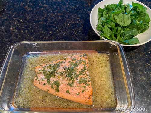 Cooked fish in a dressing with a bowl of greens at the side