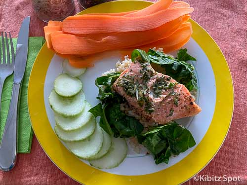 baked Salmon and Spinach served over rice with a side of carrots and cucumber on a plate