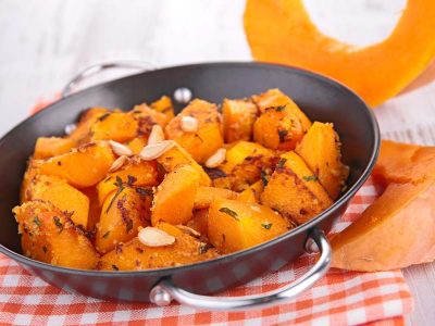 A small black pan full of roast pumpkin cubes, resting on a checkered red cloth.