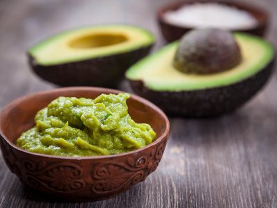Creamy Guacamole Recipe in a bowl on a wooden table, with a cut up avocado in the background