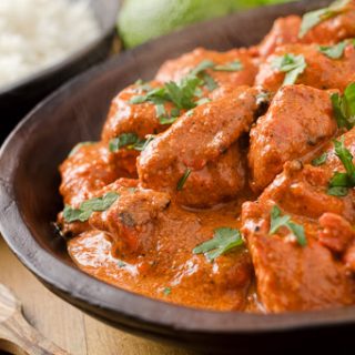 A Gluten free butter chicken recipe, topped with green herbs, with a bowl of rice in the background
