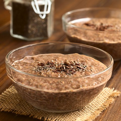 A chia chocolate pudding, topped with chia seeds and shaved chocolate, in a bowl on a woven mat.