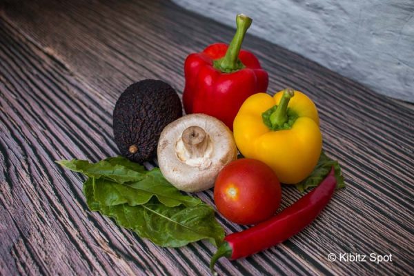 Some of the ingredients needed for Mexican fried rice, displayed on a wooden table - peppers, chilli, tomato, spinach, mushroom, and avocado