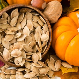 A bowl of pumpkin seeds besides a small orange pumpkin. It's a good end result photo on how to clean pumpkin seeds