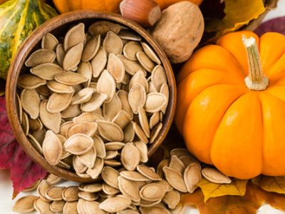 A bowl of pumpkin seeds besides a small orange pumpkin. It's a good end result photo on how to clean pumpkin seeds