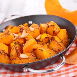 A small black pan full of roast pumpkin cubes, resting on a checkered red cloth.