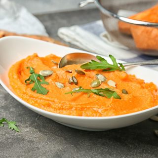 A freshly made pumpkin mash recipe in a white bowl, topped with green herbs