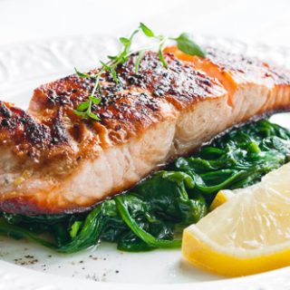 Baked salmon and spinach with a side of lemon on a white plate