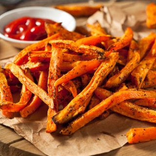 Roasted paleo sweet potato fries on a wooden board with red sauce in a bowl