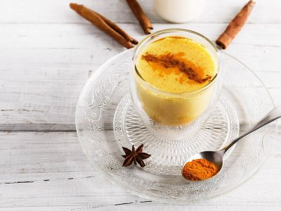 A cup of our turmeric almond milk latte, garnished with cinnamon and plated with spices on a light wooden background.