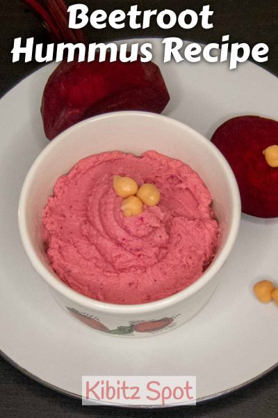 A bowl of beetroot hummus garnished with chick peas on a plate with sliced beetroot