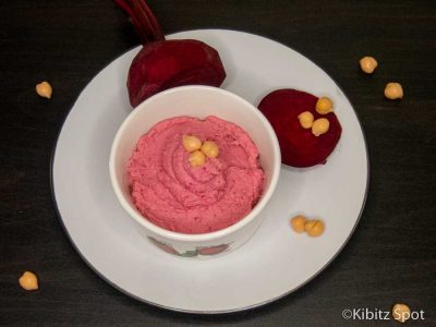 A bowl of beetroot hummus on a plate with sliced beetroot and chick peas.