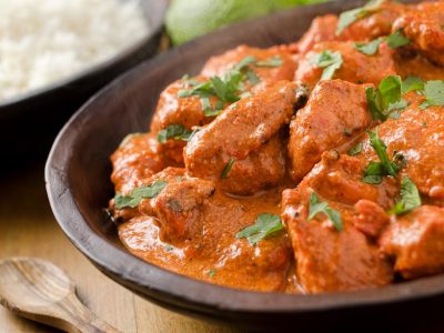 A Gluten free butter chicken recipe, topped with green herbs, with a bowl of rice in the background
