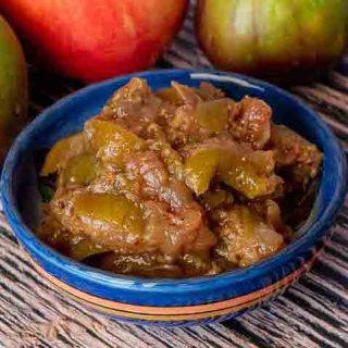 A small bowl of fig chutney with an apple and figs in the background