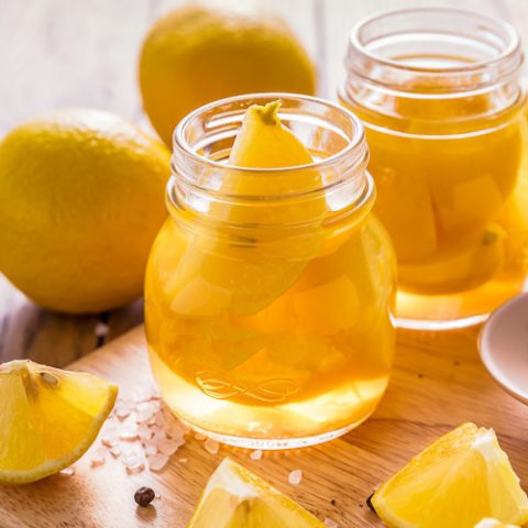 A jar of preserved lemon surrounded by ingredients used to make it