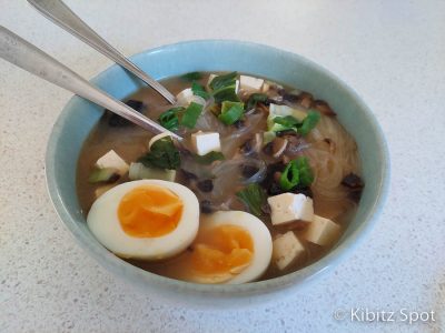 A bowl of miso soup with bok choy, tofu, mushrooms, Vietnamese noodles, scallion, and an egg