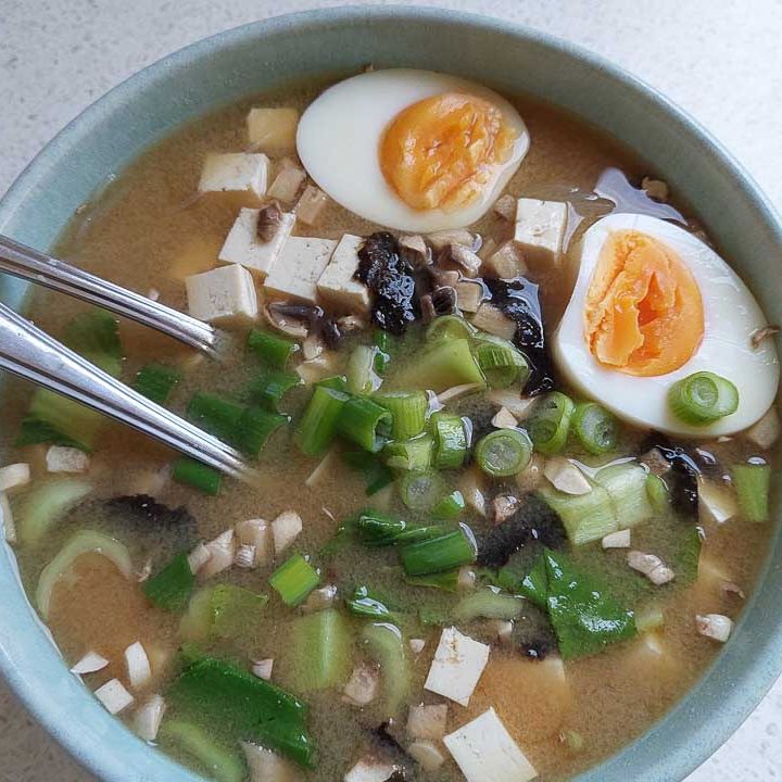 A bowl of miso soup with bok choy, tofu, mushrooms, Vietnamese noodles, scallion, and an egg