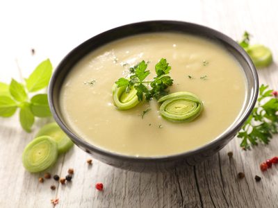 A bowl of gluten free potato leek soup garnished with parsley and sliced leeks.