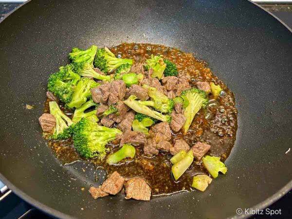 Adding the stir-fried ingredients to the thickened sauce to coat everything